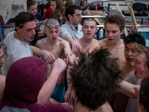Swimmers huddle together in advance of a swim meet with Danny Lynam, award-winning coach at the center